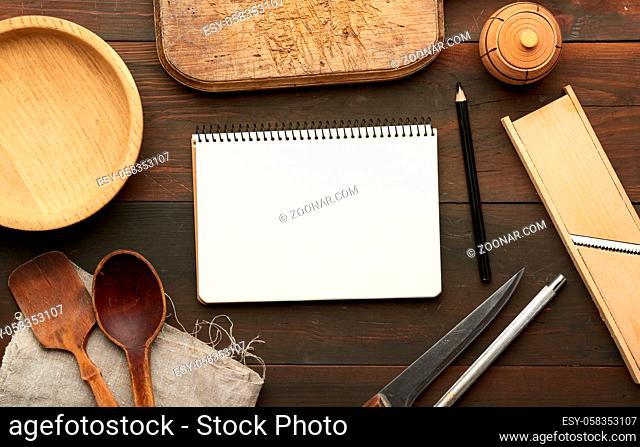 open notebook with blank white sheets and kitchen utensils on brown wooden table, top view