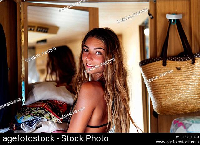 Woman looking over shoulder while holding clothes inside motor home