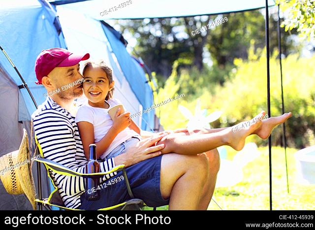 Happy, affectionate father holding daughter in lap at sunny campsite