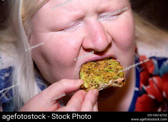 Woman eating a slice of avocado toast with her eyes closed