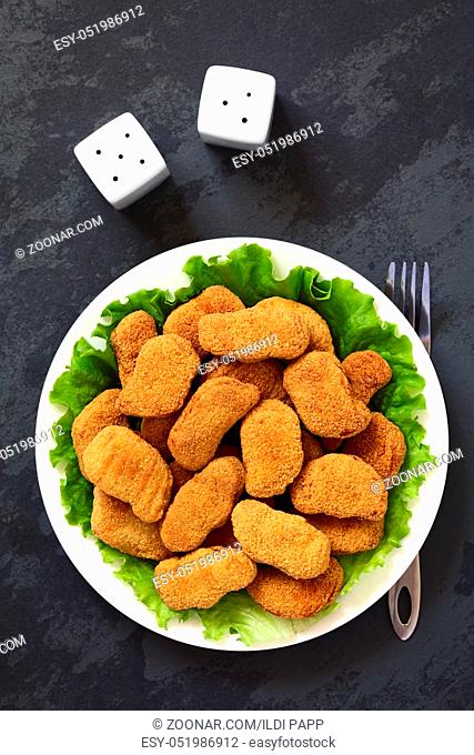 Fried breaded crispy chicken nuggets on lettuce leaves on plate, photographed overhead on slate with natural light
