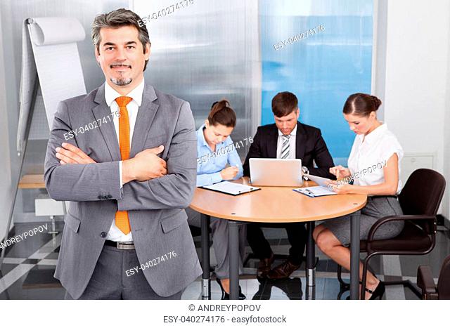 Successful Businessman With Arm Crossed Standing In Front Of His Colleagues
