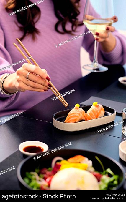 Mature woman having sushi with chopsticks at restaurant