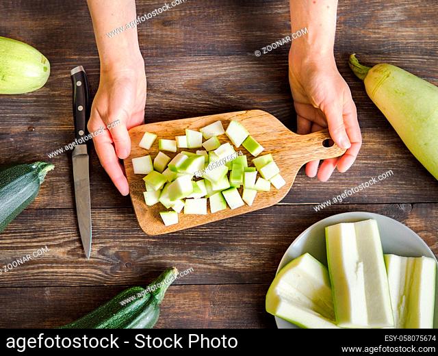 Zucchini harvest. Woman slices zucchini cubes for freezing on wooden table. Farm organic zucchini harvesting Top view or flat lay