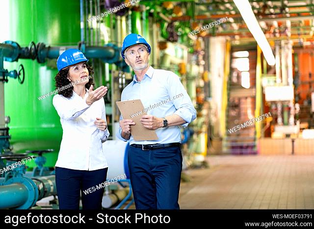 Professional team with hardhat discussing while checking machine at power station