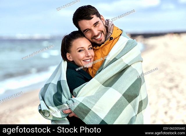happy couple in warm blanket on autumn beach