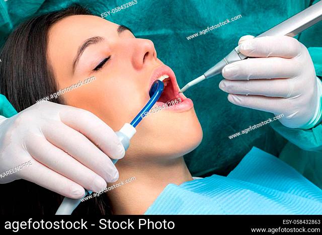 Close up macro face shot of young woman having dental cleaning.Hands wearing gloves working on teeth with saliva ejector and water cleaning unit