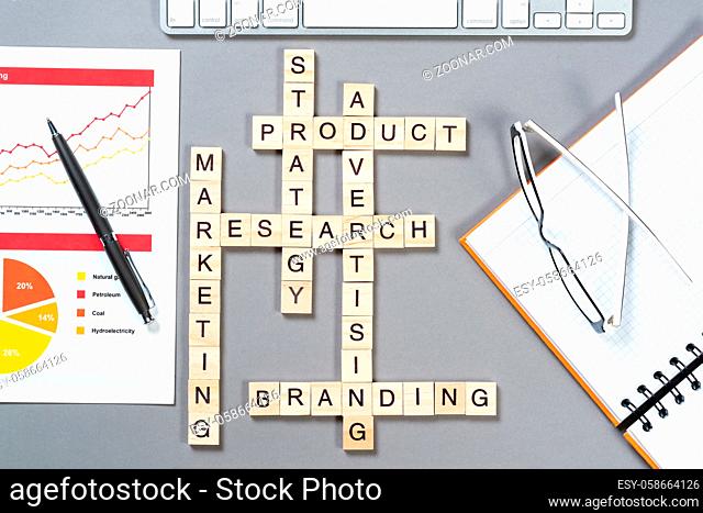 Product branding concept with words from cubes. Still life of office workplace with crossword. Flat lay grey surface with computer keyboard and infographics