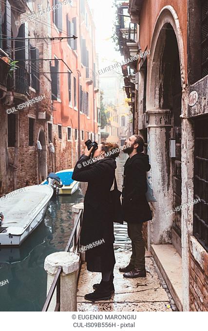 Couple photographing building exteriors from canal waterfront, Venice, Italy