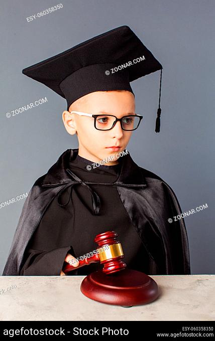 Portrait of serious smart child in graduation cap playing in judge. Boy dream about future profession