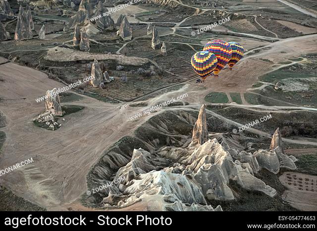 Three multi-colored air balloons are standing on the ground in the valley. They are preparing to fly. Balloons colored in red, blue, yellow, orange, green, gray
