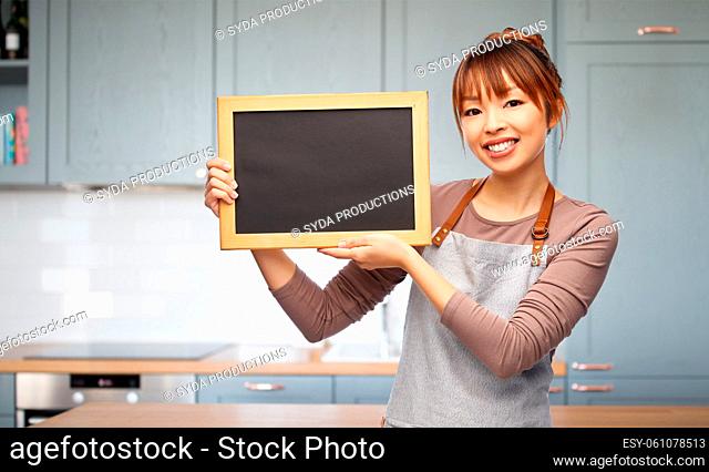happy woman in apron with chalkboard in kitchen