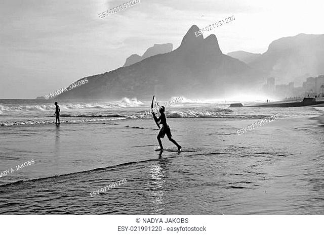 Teenager springt mit Surfbrett ins Wasser am Strand von Ipanema