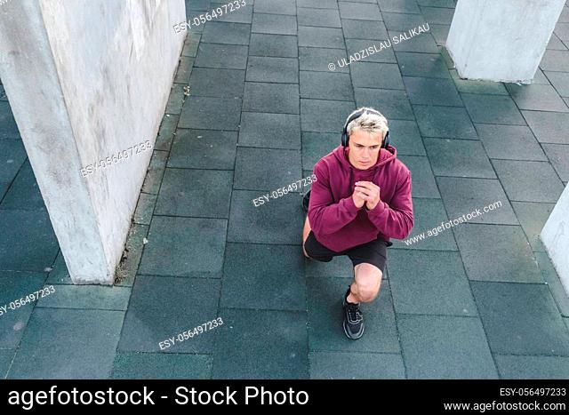 Young athletic man with headphones listen to music and warming up outdoors. Do lunge