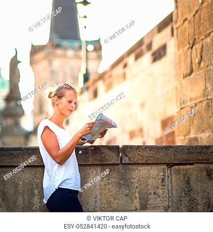 Pretty young female tourist studying a map, enjoying discovering a new city, looking excited (shallow DOF; color toned image)