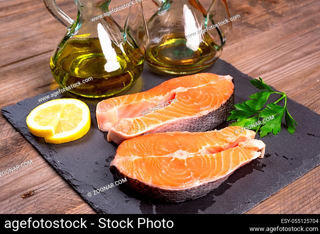 Delicious salmon steak on wooden table with lemon, parsley and olive oil, close-up