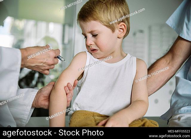 Pediatrist injecting vaccine into arm of unhappy toddler