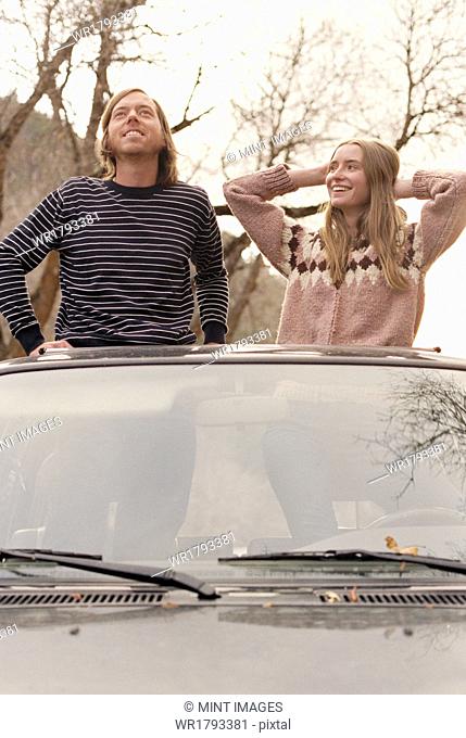 Young couple standing in their car, looking through sunroof