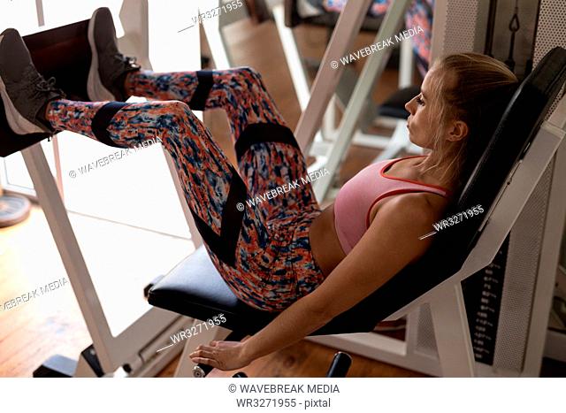 Female boxer exercising on leg press machine in fitness studio