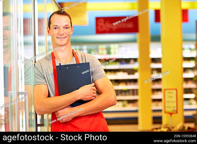 Lächelnder Verkäufer mit Klemmbrett lehnt am Kühlregal im Supermarkt