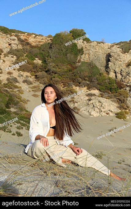 Contemplative woman with long hair sitting on sand at beach, Patara, Turkiye