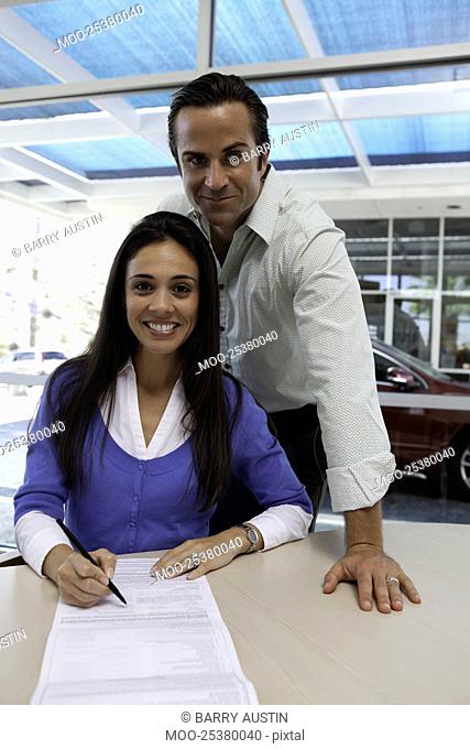 Portrait of woman signing car contract with husband standing behind