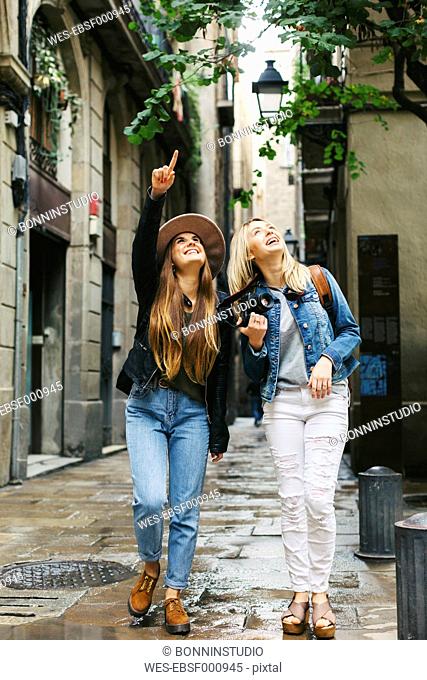 Spain, Barcelona, two young women walking in the city looking up