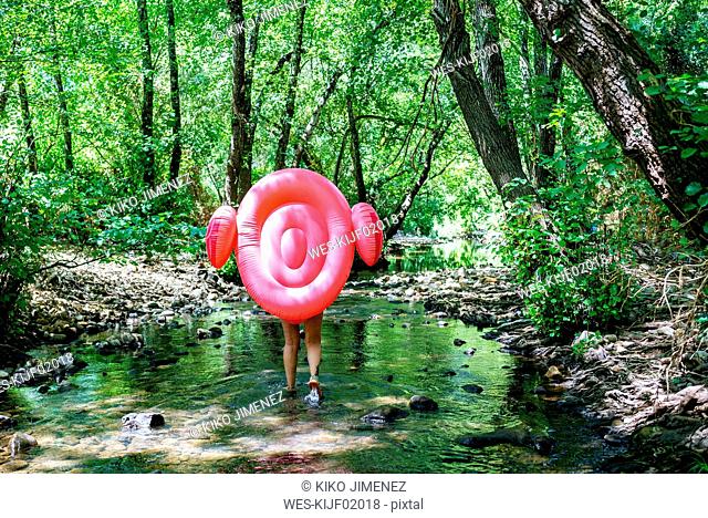 Woman walking in river, carrying an inflatable flamingo