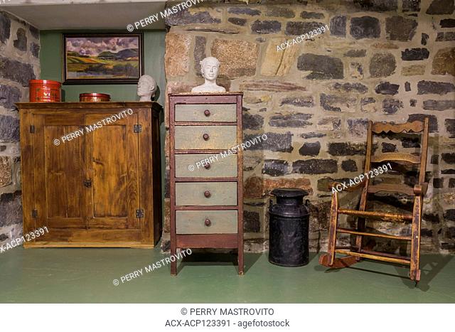 Antique wooden armoire, chest of drawers and rocking chair against a fieldstone wall in the basement inside an old circa 1805 Canadiana cottage style home
