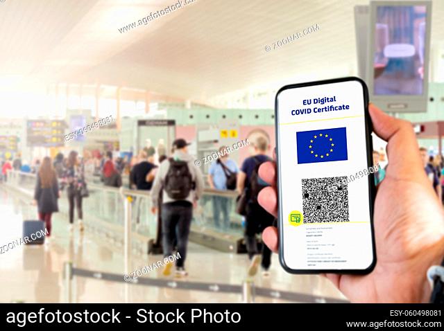 EU Digital COVID Certificate with the QR code on the screen of a mobile held by a hand with blurred airport in the background. Immunity from Covid-19