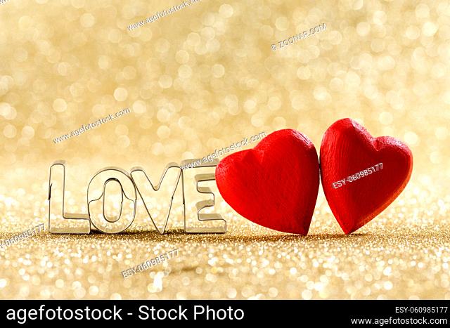 Two red handmade wooden hearts and word love on golden bright glitter lights bokeh background