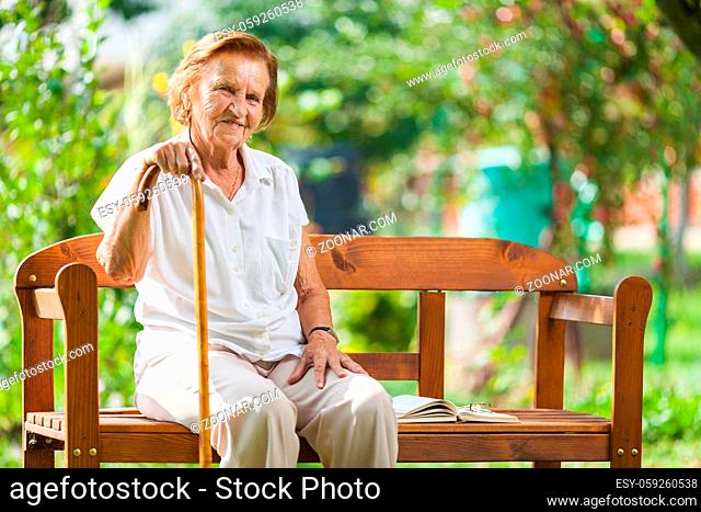 Elderly woman sitting and relaxing on a bench outdoors in park