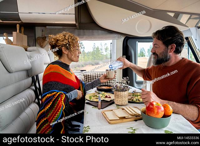 Adult couple enjoy time eating inside camper van in mountain holiday free vacation together. Man and woman in vanlife or tourist activity inside rv motorhome