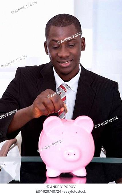 Businessman Inserting Coin In Piggybank