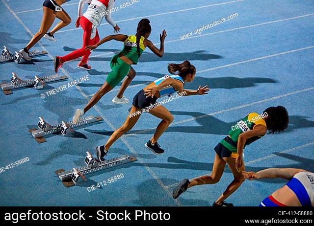 Female track and field athletes taking off from starting blocks