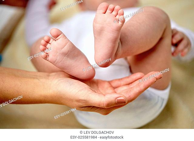 family, motherhood, parenting, people and child care concept - close up of newborn baby feet in mother hands