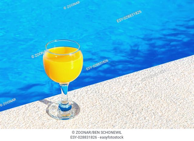 Glass with orange juice on edge of swimming pool