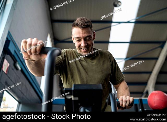 Smiling male athlete exercising on cross trainer in gym