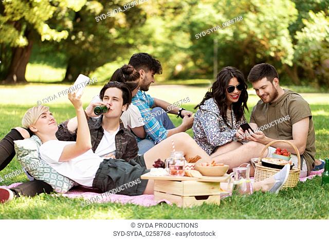 friends with smartphones on picnic at summer park
