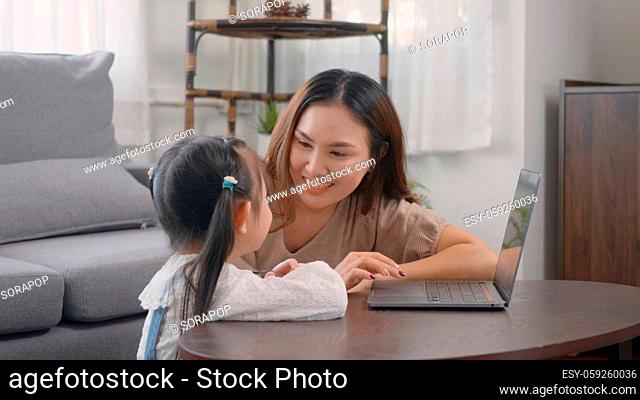 Asian young mother with laptop computer teaching her kid to learn or study online in living room at home, Mum and little preschool daughter learning online on...