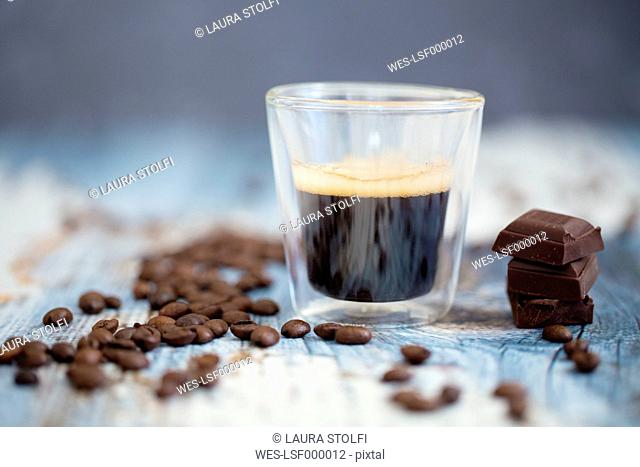 Glass cup of espresso, roasted coffee beans and dark chocolate on wood