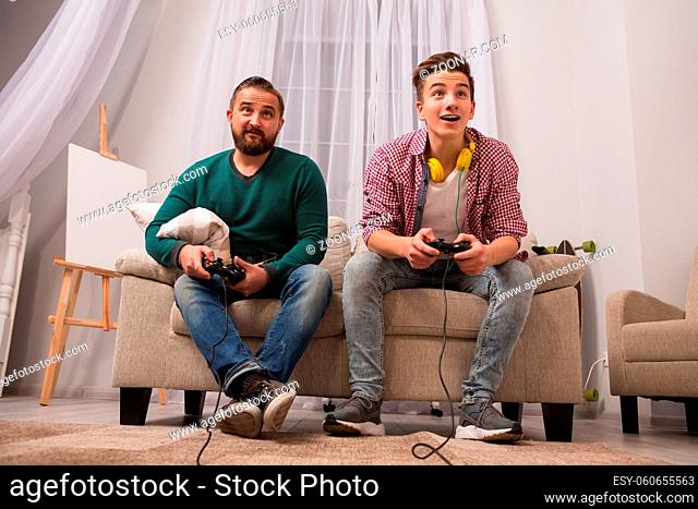 Father and son playing in the console at home. Concept of popularization of video games