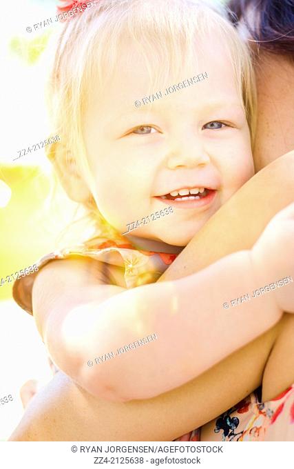 Bright summer portrait of happy cute child girl hugging mum in the glare of a morning sunrise