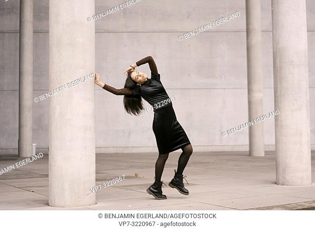 sensitive emotional woman dancing between tall pillars, architecture, fashionable clothes, in city Munich, Germany