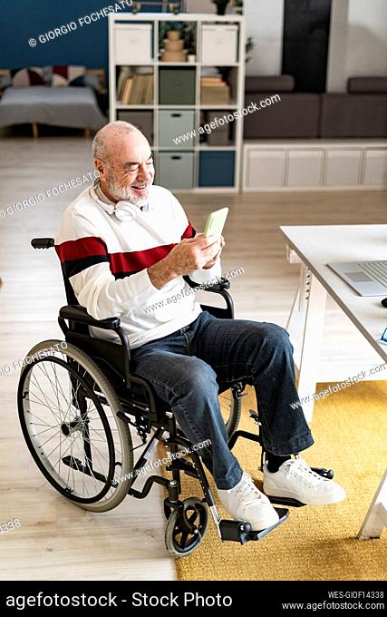 Smiling disabled man with headphones using mobile phone at home office