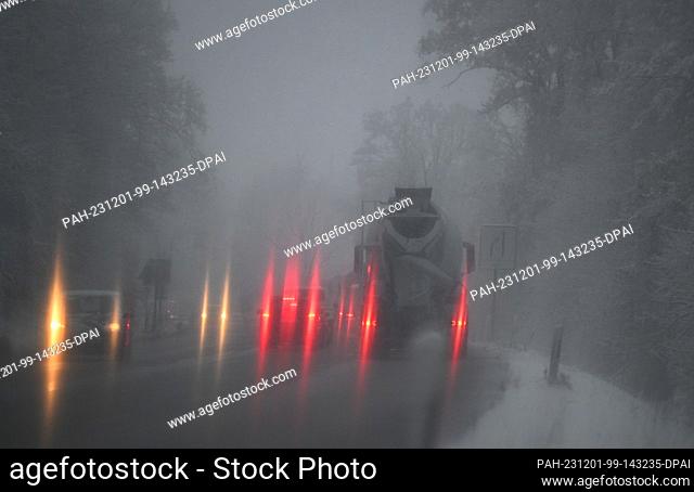 01 December 2023, Baden-Württemberg, Stuttgart: Rear lights of vehicles shine through a snow-covered windshield during the morning rush hour