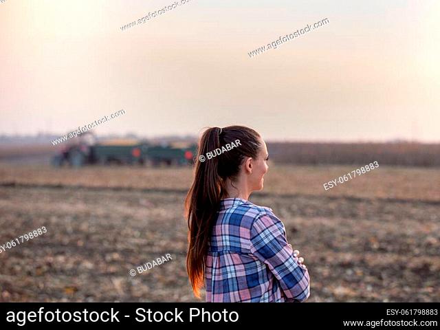 Rear view of farmer woman standing in corn field during harvest with tractor in background