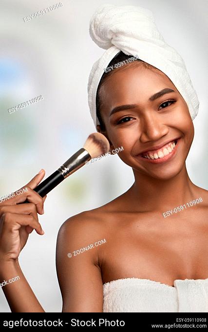 Close-up portrait of a beautiful smiling woman with clean skin holding makeup brush isolated on bright background. Beauty treatments and cosmetics spa therapy
