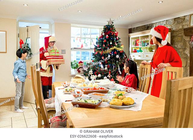 Chinese family at Christmas time. The son is opening the door to his Dad who is dressed like Father Christmas and bearing gifts