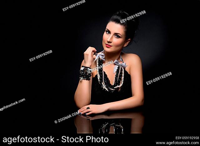 Portrait of beautiful young woman with shiny black hair and bright makeup sitting near glass table. Over dark background. Copy space